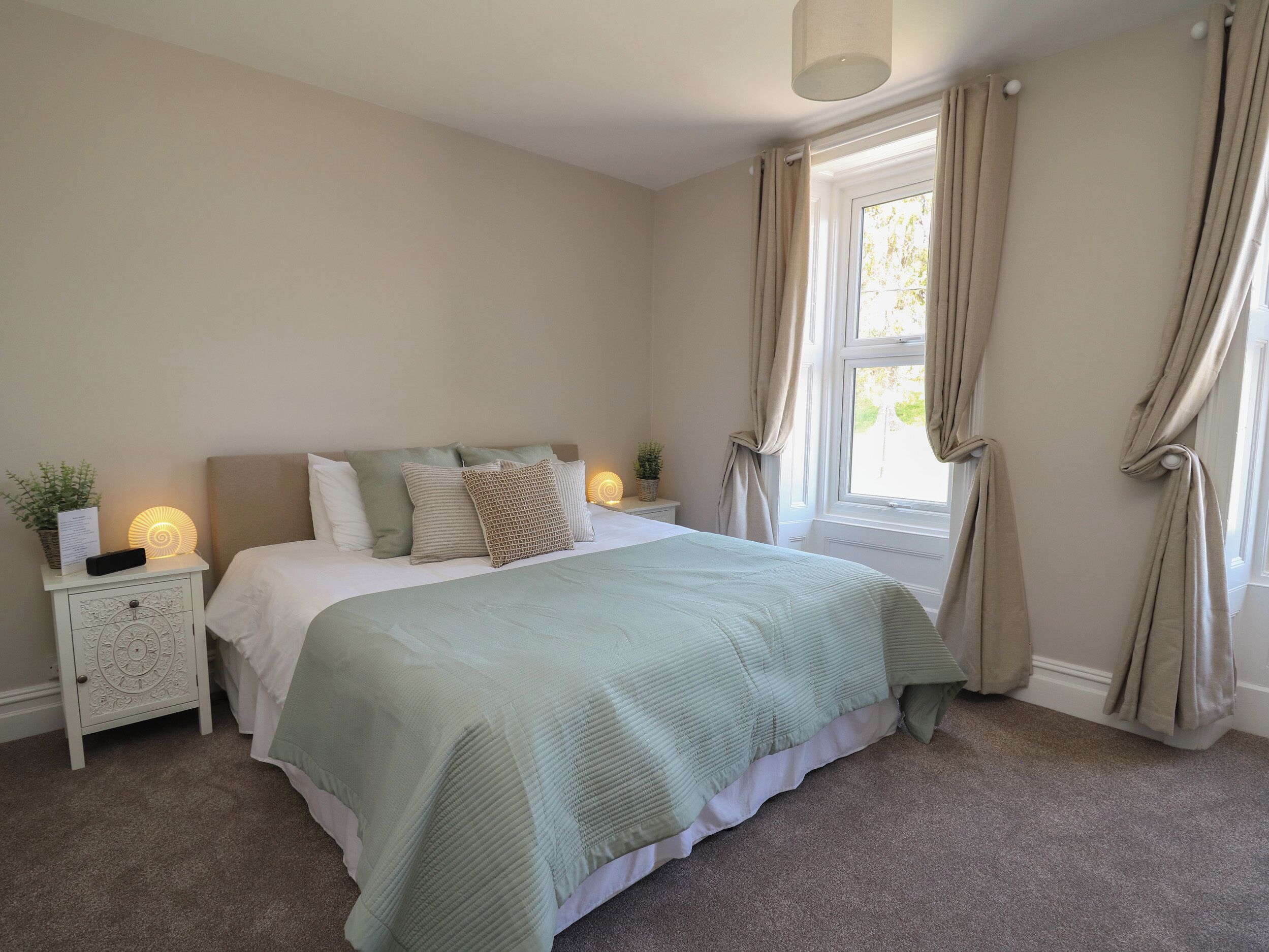 A neatly arranged bedroom with a bed, bedside tables, and a window with curtains.