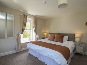 Une chambre à coucher avec un grand lit, deux lampes de chevet, une fenêtre avec des rideaux et un radiateur.