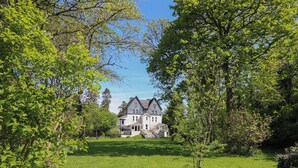 Una grande casa storica con facciata simmetrica, immersa nel verde e circondata da un prato curato.