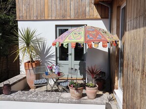 A patio with a table and chairs, potted plants, and a colorful umbrella. - Little Sea Thrift (Lyme Regis)