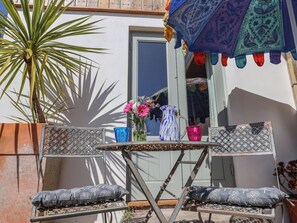 A small outdoor seating area with a metal table and two chairs, a potted plant, and a colorful umbrella. - Little Sea Thrift (Lyme Regis)