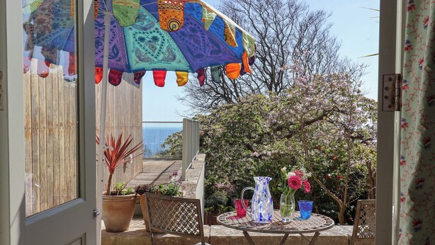 Een terras met een tafel en stoelen, een kleurrijke parasol en plantenbakken.