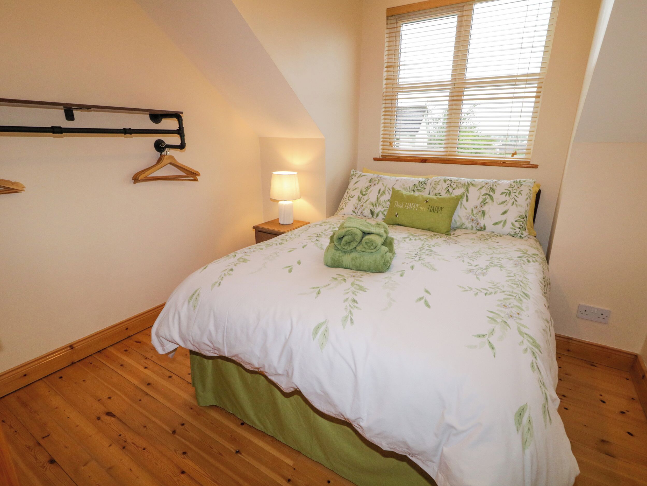 Een slaapkamer met een bed, een bedlampje, een raam met zonwering en een houten vloer.