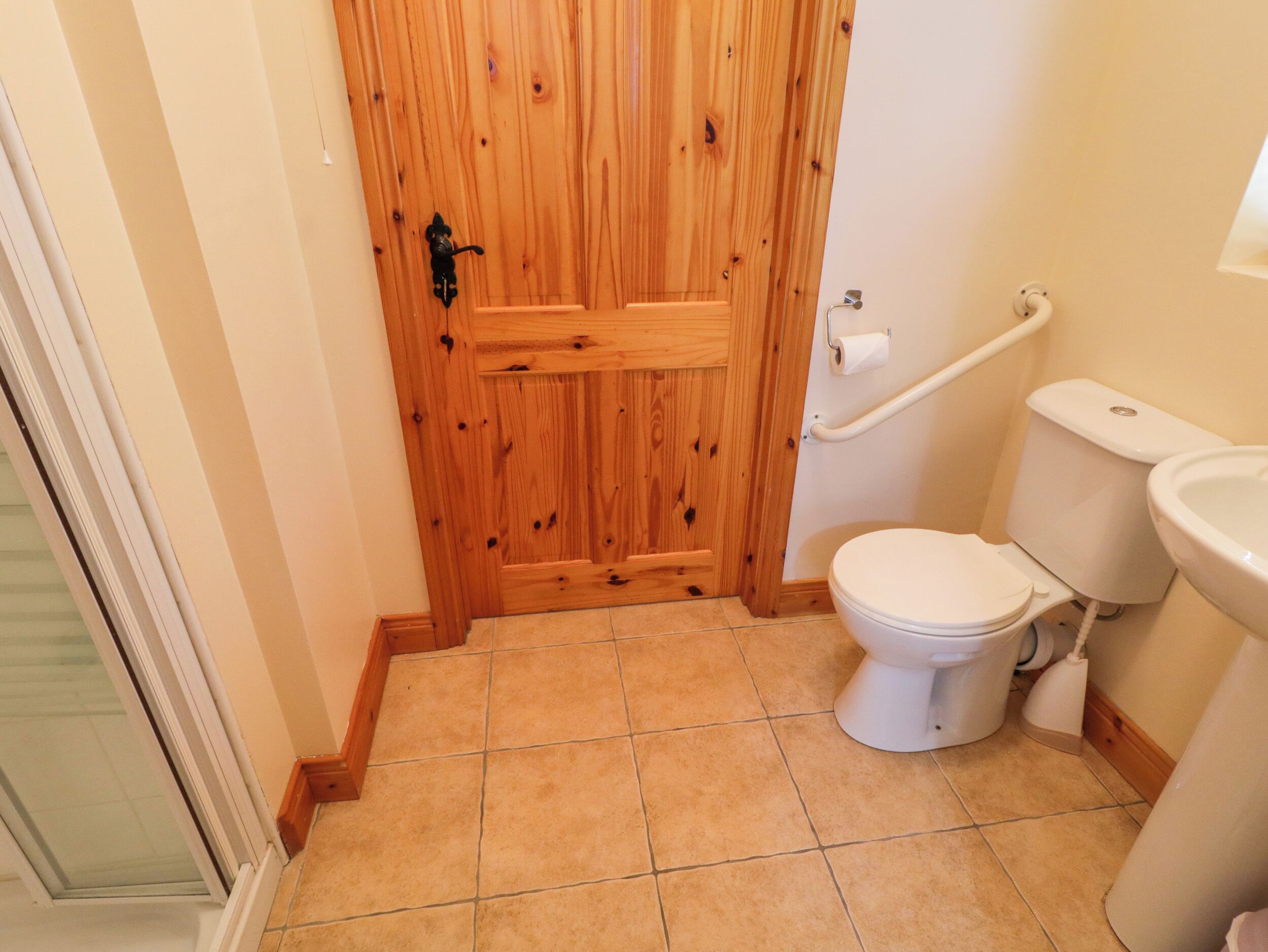A bathroom with a wooden door, a white toilet, a bidet, and a handrail.