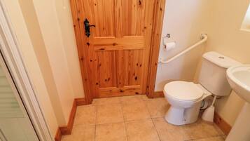 A bathroom with a wooden door, a white toilet, a bidet, and a handrail.