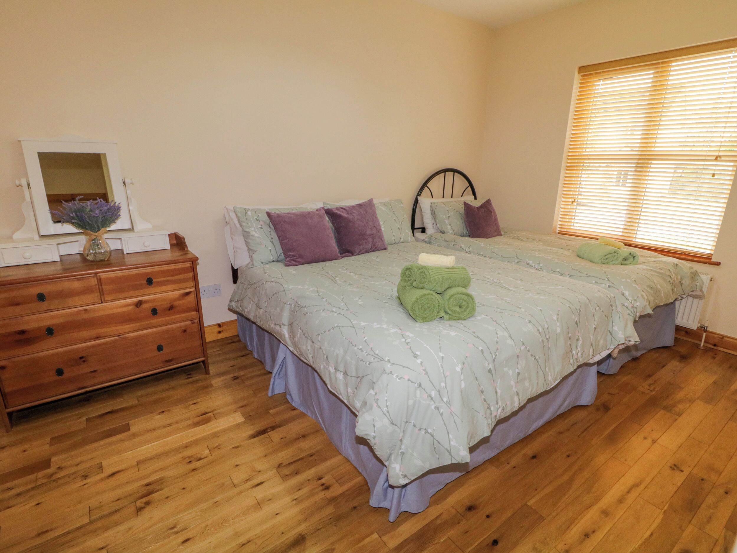 A bedroom with a bed, wooden dresser, and a window with blinds.