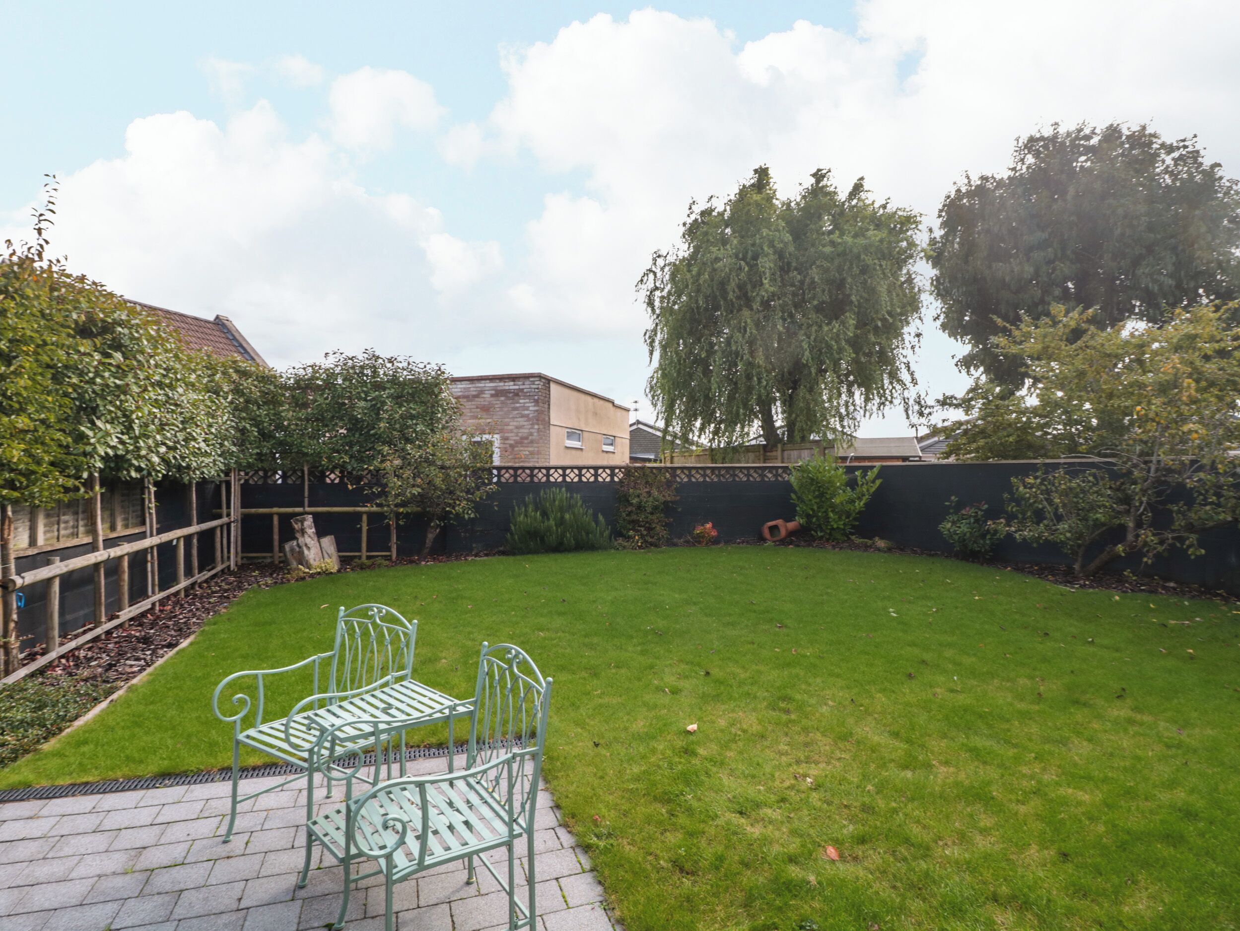 A backyard with a lawn, a metal bench, and a brick pathway.