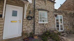 A stone cottage with a white door, a window with shutters, and a sign that reads "Rose Cottage". - Rose Cottage (Scarborough)