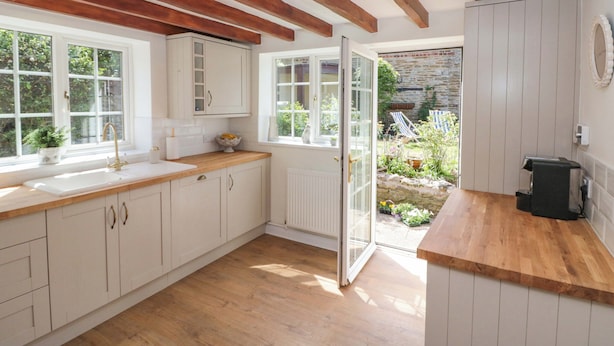 A kitchen with wooden beams, white cabinets, and a view to a garden. - Rose Cottage (Scarborough)