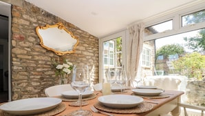 A dining area with a stone wall, a mirror, and a table set for four with plates, glasses, and cutlery. - Rose Cottage (Scarborough)