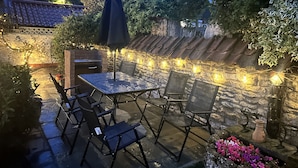 An outdoor patio with a stone wall, a grill, and string lights. - Rose Cottage (Scarborough)