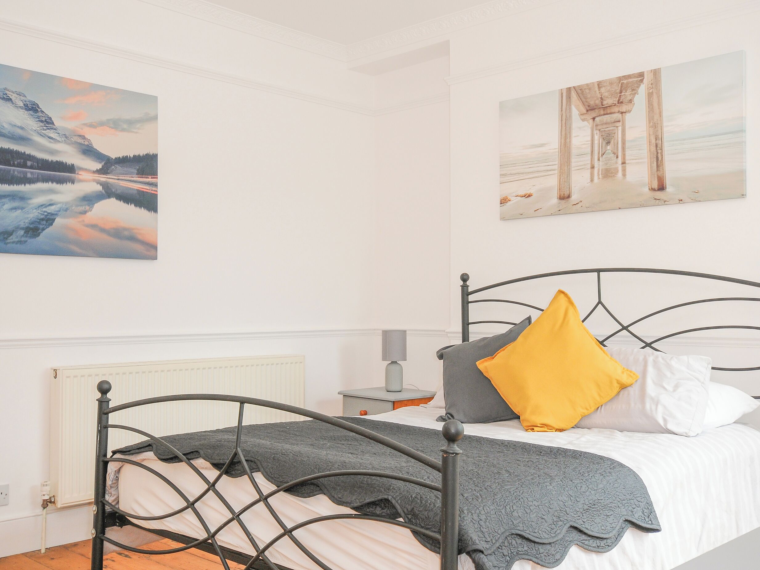 A bedroom with a metal bed frame, white bedding, and two paintings on the walls.