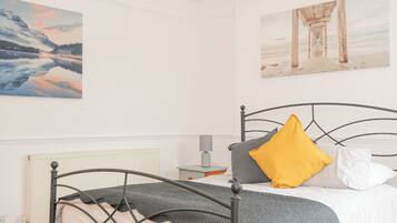 Un dormitorio con estructura de cama metálica, ropa de cama blanca y dos cuadros en las paredes.