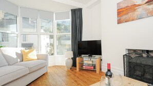 A living room with a sofa, a television, a fireplace, and a table with wine glasses. - Albert House (Looe)