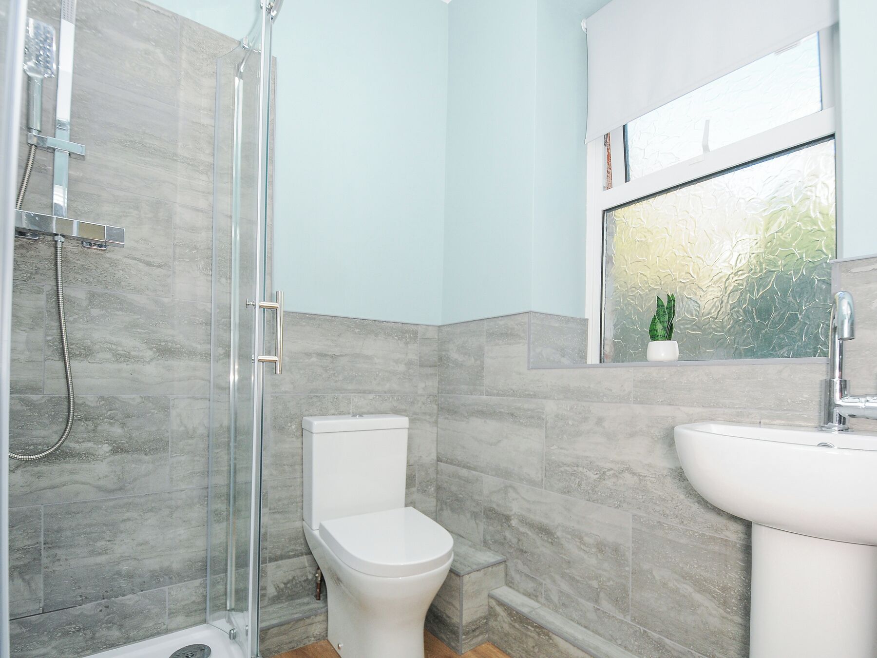 Un baño con ducha, inodoro, lavamanos y ventana con vistas al verdor.
