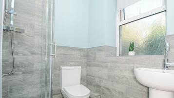 Un baño con ducha, inodoro, lavamanos y ventana con vistas al verdor.