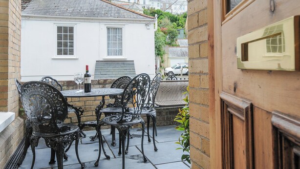 A patio with outdoor seating and a table set with a bottle and glasses. - Albert House (Looe)