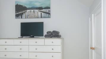 A bedroom with a white dresser, a flat-screen TV, and a painting of a pier.