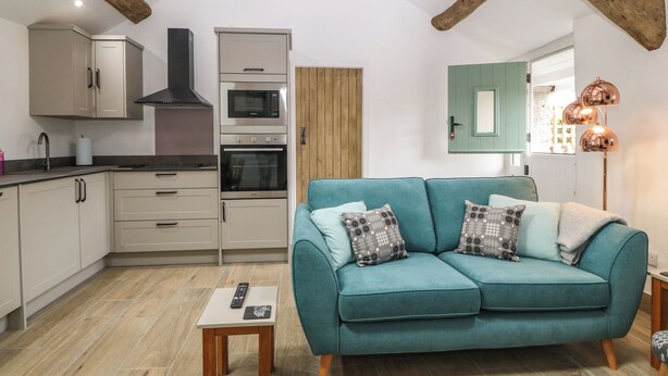 A modern kitchen with built-in appliances, a teal sofa, and a wooden ceiling. - Y Stabl (Dyffryn Ardudwy)