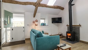 A cozy living room with a teal sofa, a fireplace, a TV mounted on the wall, and a wooden ceiling beam. - Y Stabl (Dyffryn Ardudwy)
