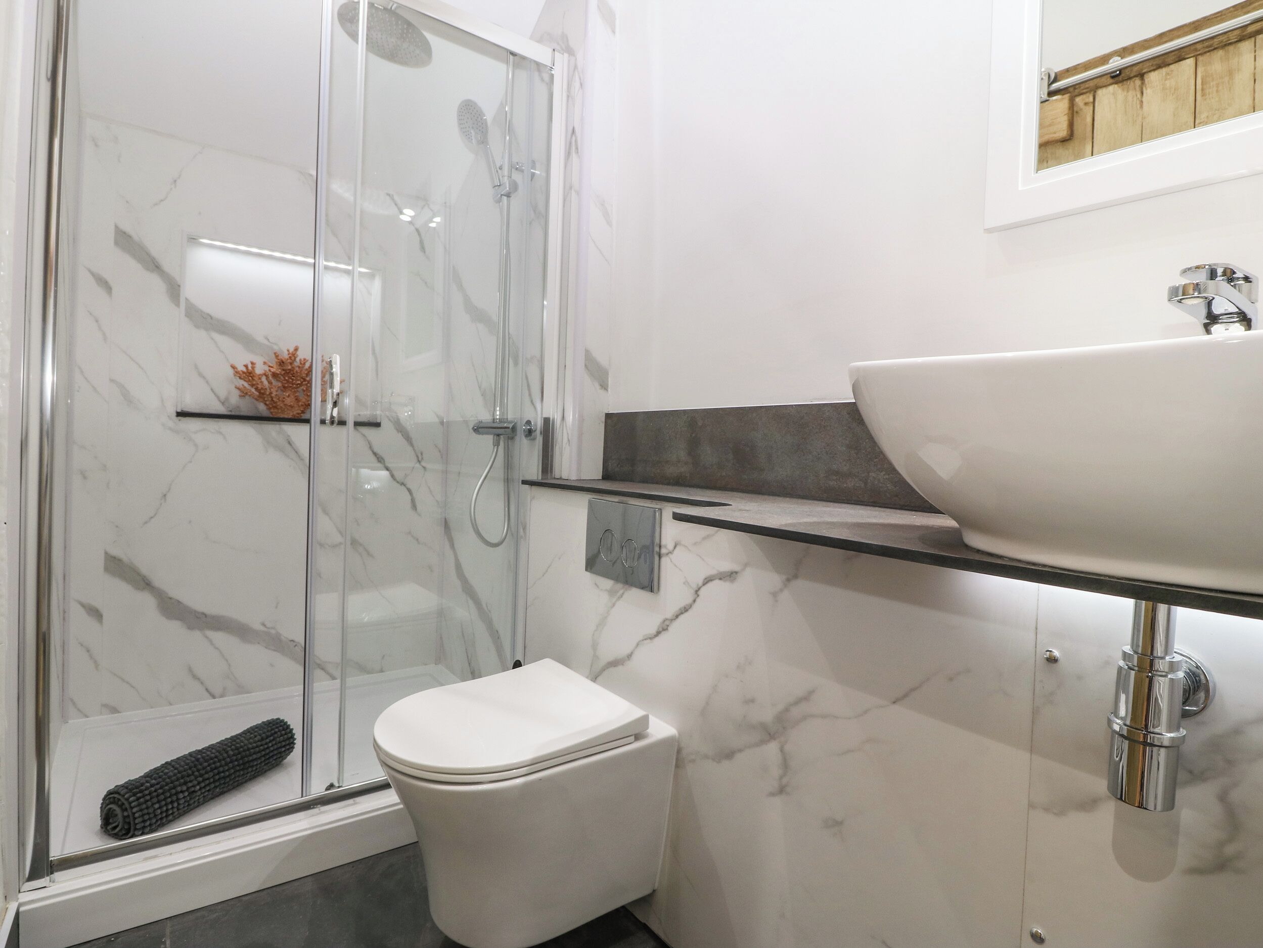 A modern bathroom with a glass-enclosed shower, a white toilet, and a marble-tiled sink area.