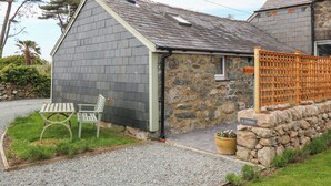 A stone building with a sloped roof, a chimney, and a wooden fence. - Y Stabl (Dyffryn Ardudwy)