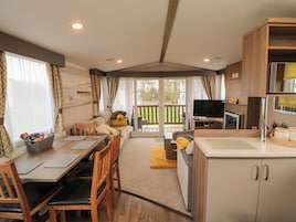 Amplia sala de estar con sofá, mesa de comedor y sillas. Hay un televisor y una zona de cocina con armarios y un lavabo.
