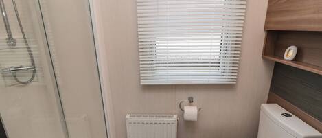 Baño compacto con cabina de ducha de vidrio, inodoro y radiador.