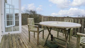 A wooden deck with a round table and two chairs, a glass door, and a view of the sky and clouds. - Tan Y Ffordd (Pwllheli)
