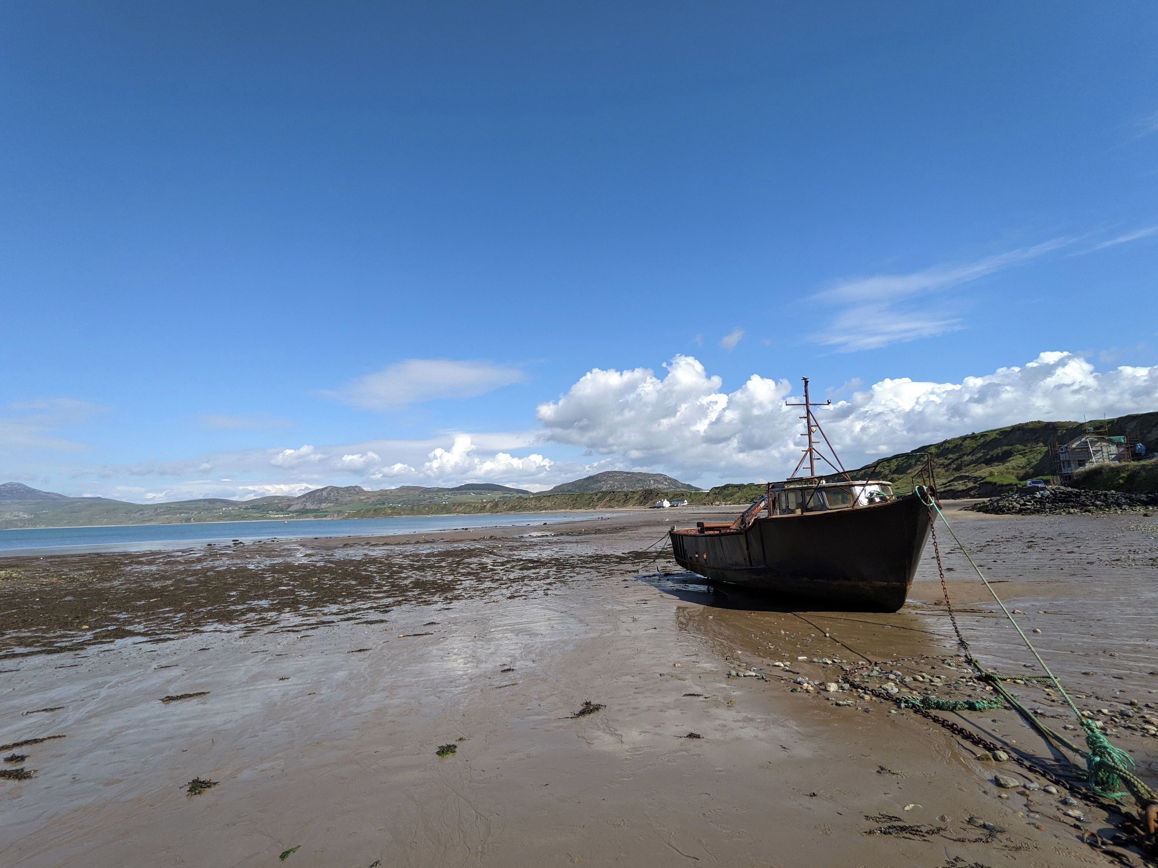 Ein Boot am sandigen Strand, bewölkter Himmel und Hügel in der Ferne.