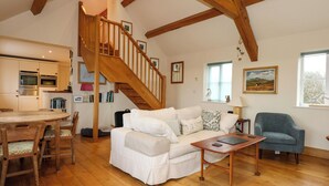 A spacious living area with a wooden staircase, a white sofa, a dining table with chairs, and a kitchen in the background. - Tan Y Ffordd (Pwllheli)
