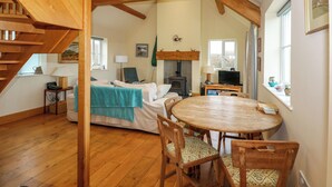 A cozy room with a wooden staircase, a bed with a blue blanket, a round wooden table with chairs, a television, and a fireplace. - Tan Y Ffordd (Pwllheli)