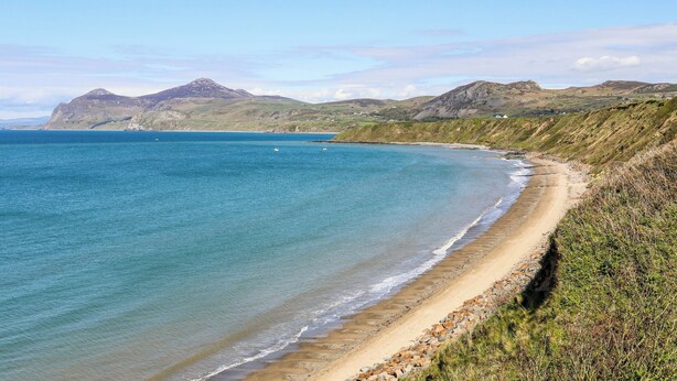 A coastal landscape with a sandy beach, rocky outcrops, and distant hills under a clear sky. - Tan Y Ffordd (Pwllheli)