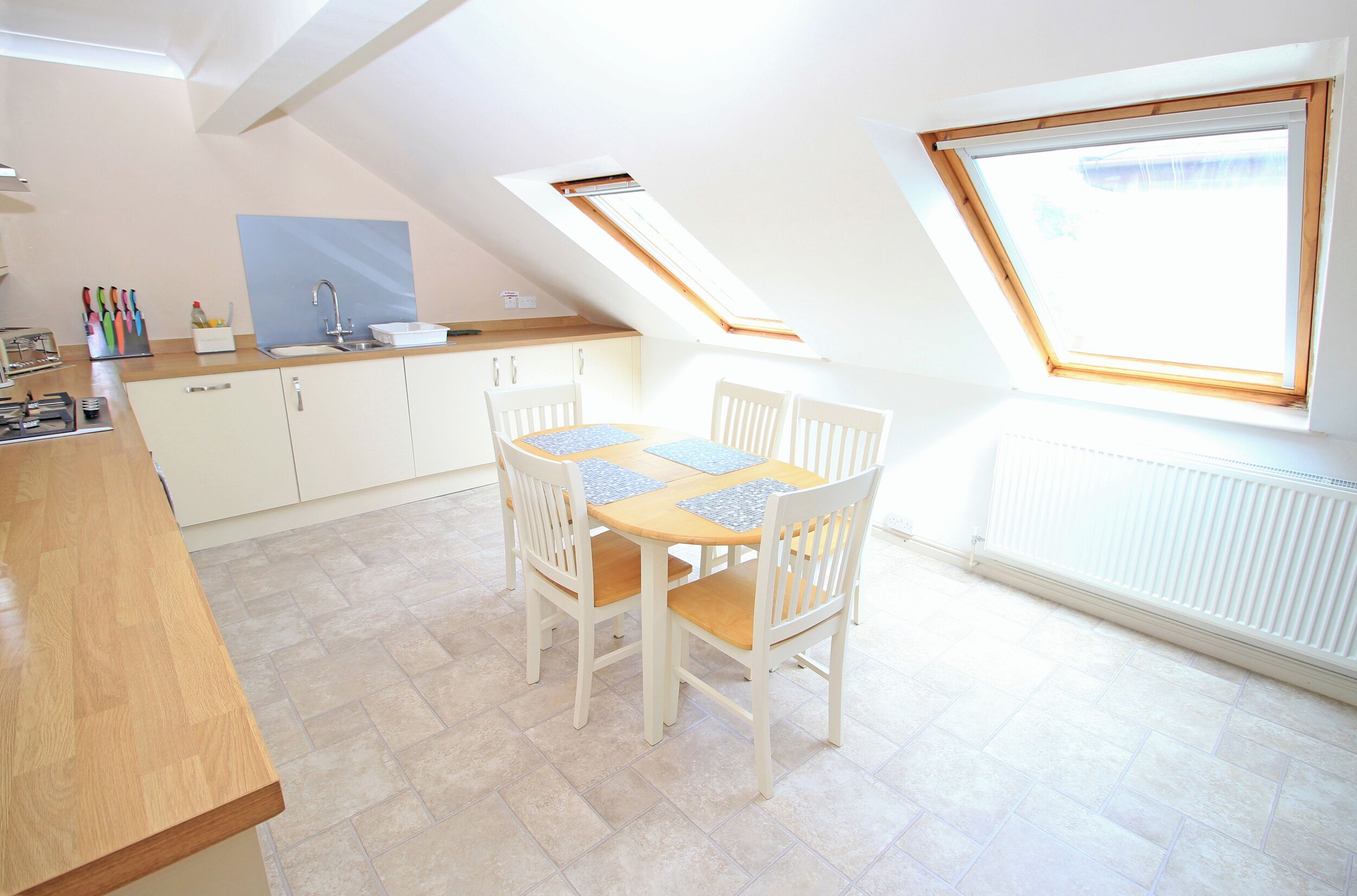 A kitchen with a dining table, chairs, a window, and a skylight.
