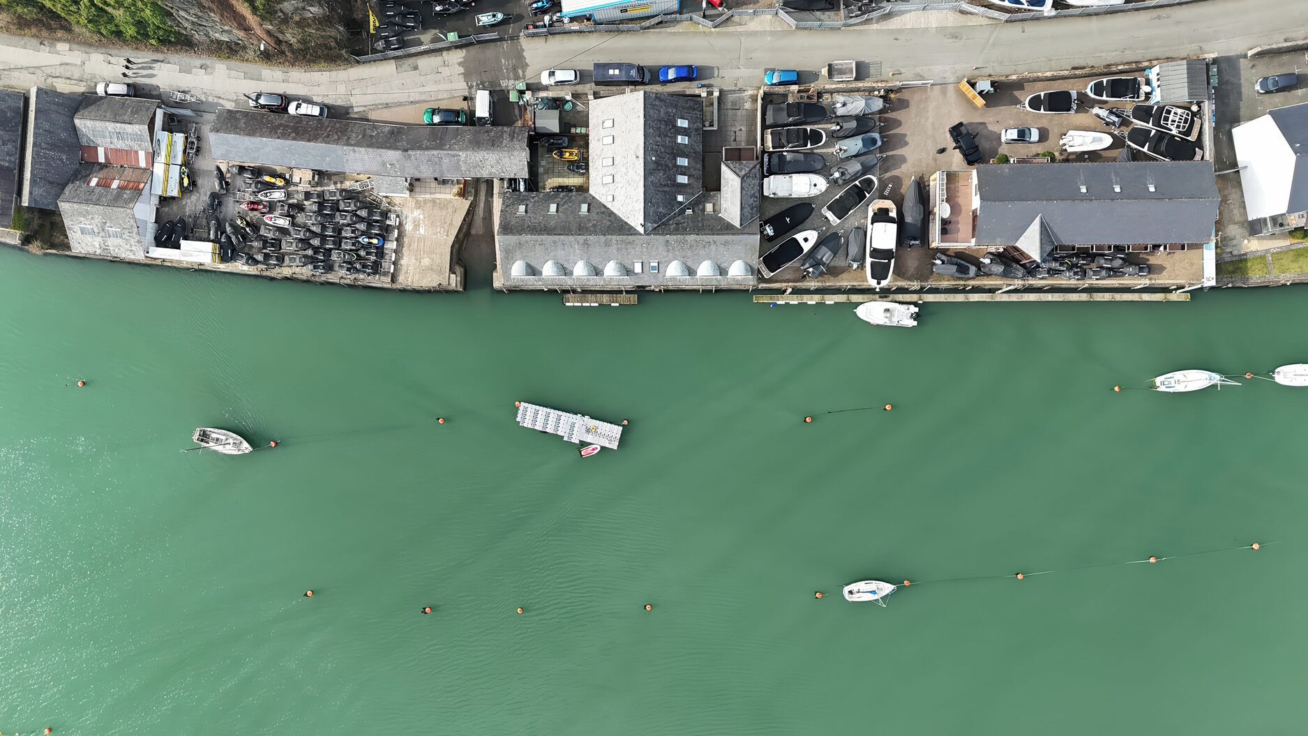 Vista aérea de un puerto deportivo con barcos amarrados y un pequeño muelle que se adentra en el agua.