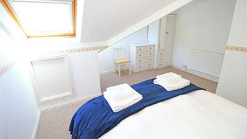 A bedroom with a skylight, a bed with a blue blanket, a chair, a dresser, and a mirror.