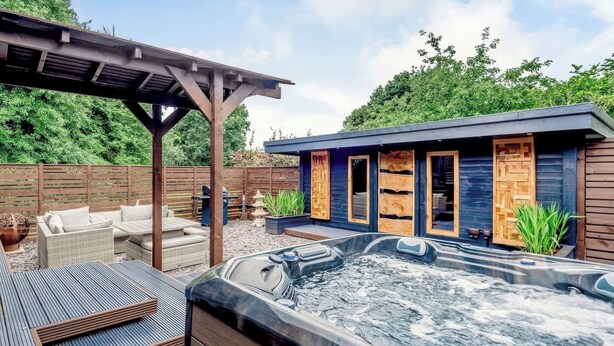 Un espace avec un jacuzzi, agrémenté d’une pergola, de sièges extérieurs et d’une structure en bois dotée de fenêtres.