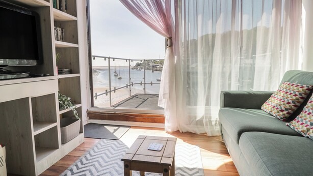 A living room with a television, bookshelves, a sofa, and a view of the sea through a window.