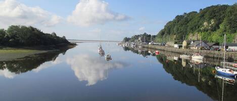 A calm harbor with boats docked along the quay, surrounded by greenery and buildings.