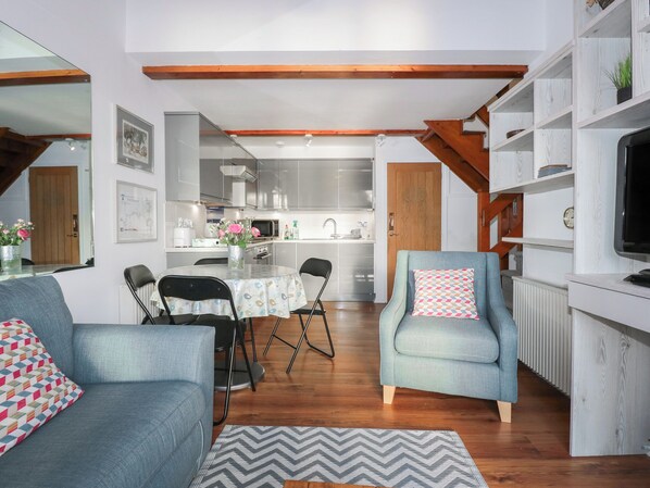 A modern living room with a dining area, wooden beams, a kitchen in the background, and a television on a wooden stand.