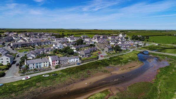 Un village côtier avec des maisons le long du rivage, un pont qui relie la région et une petite plage où sont amarrés des bateaux.