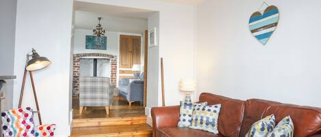 A living room with a brown leather sofa, a plaid armchair, and a colorful armchair. A fireplace is visible in the background, and there is a heart-shaped decoration on the wall.