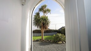 Une porte qui donne sur un jardin agrémenté d’un palmier, d’une haie et d’un mur en pierre.