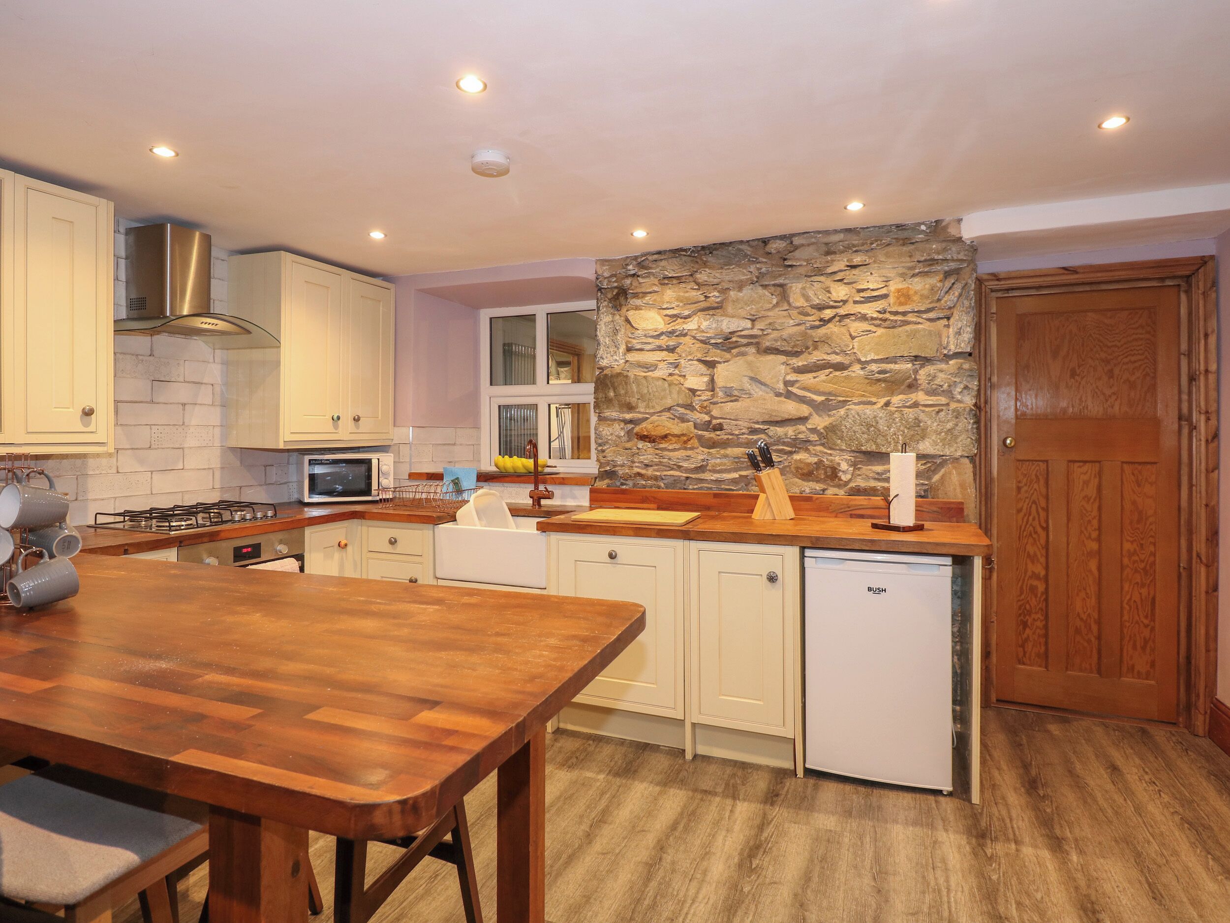 A kitchen with white cabinets, a stone accent wall, a wooden dining table, and a built-in dishwasher.