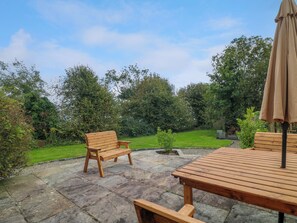 An outdoor patio with wooden furniture, including a bench and a table, set on stone tiles. - Seaforest Lodge (Gorey)