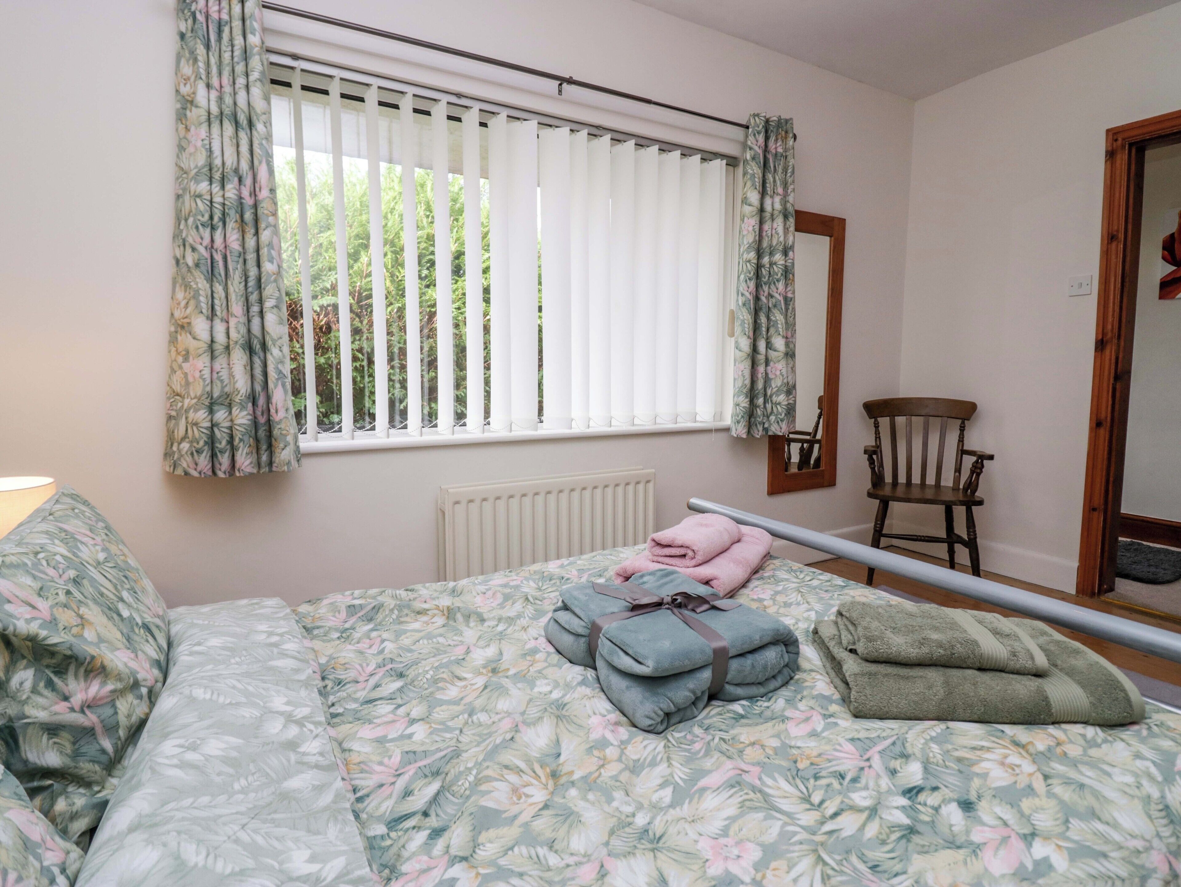 A bedroom with a bed, a chair, a window with curtains, and a radiator.