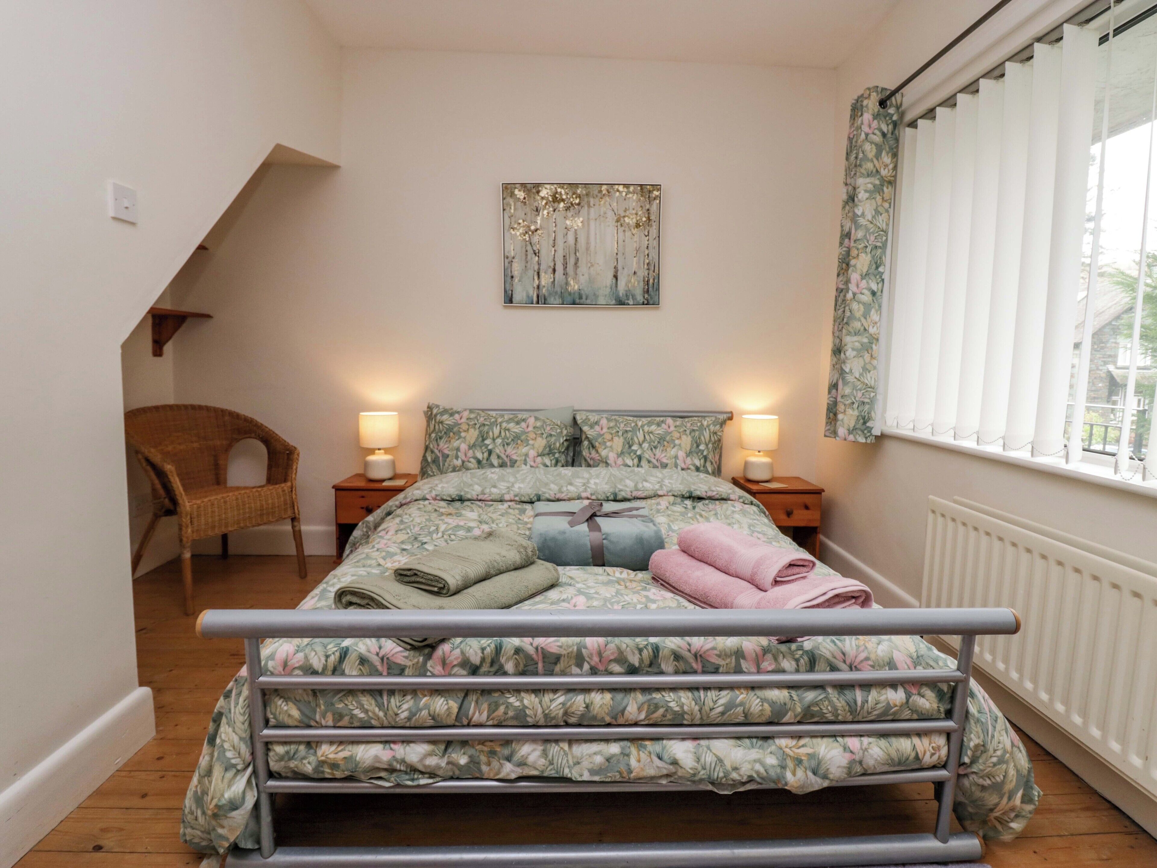 Une chambre à coucher comprenant un lit, deux tables de chevet, une chaise, une fenêtre avec des rideaux et un radiateur.