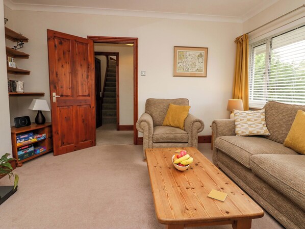 A living room with a wooden door, a staircase, a sofa, a coffee table with fruit, and a bookshelf. - Lyndhurst (Ambleside)