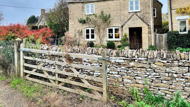 A stone house with a wooden gate, a stone wall, and a garden with autumn foliage. - Meadow View Cottage (Cheltenham)