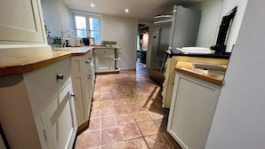 A narrow kitchen with white cabinets, a tiled floor, and a stainless steel refrigerator. - Meadow View Cottage (Cheltenham)